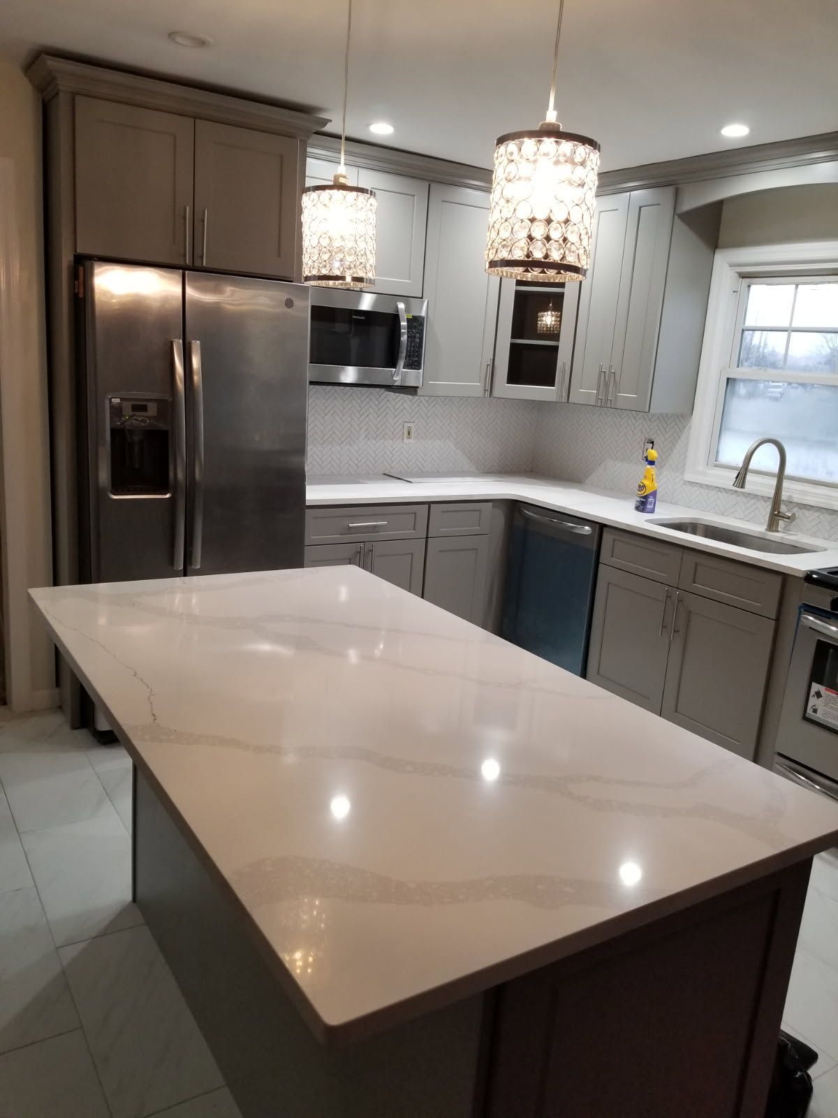 Gray and white kitchen with island, stainless steel appliances, and two hanging chandeliers.