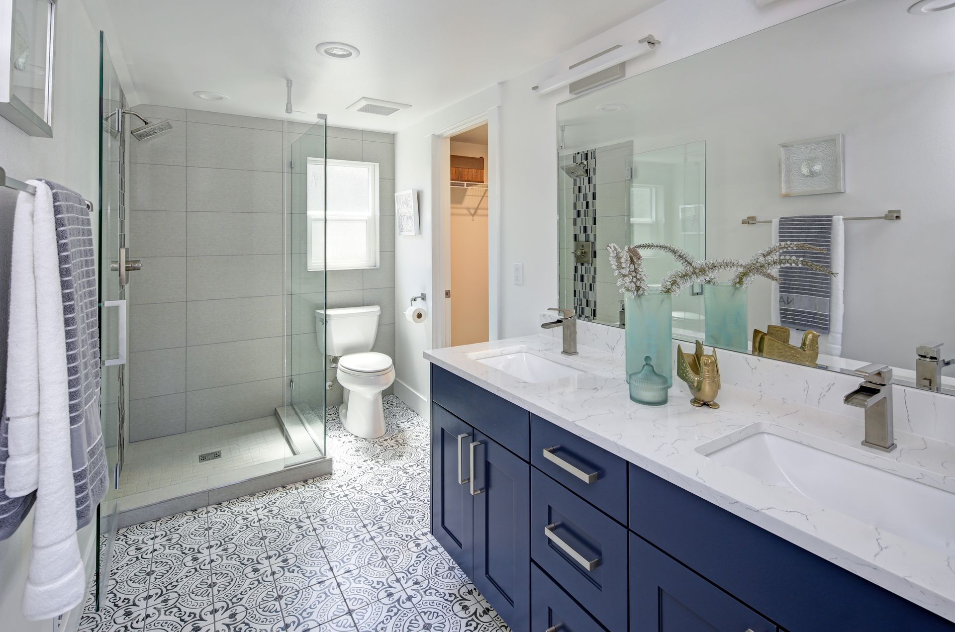 Bright modern bathroom with glass shower, navy vanity, white tile, and patterned floor.