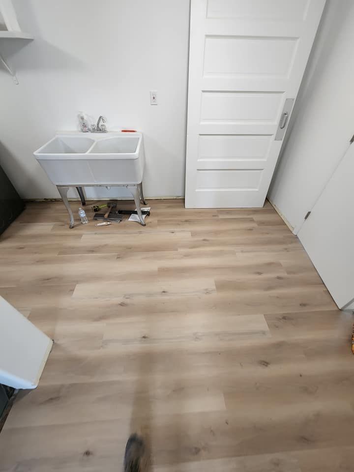 A laundry room with a sink and a wooden floor.
