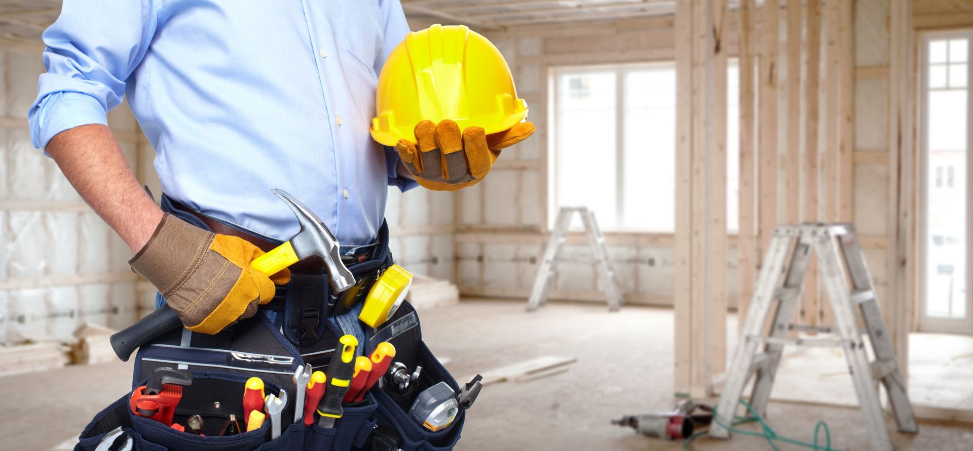 A construction worker is holding a hard hat and a tool belt.