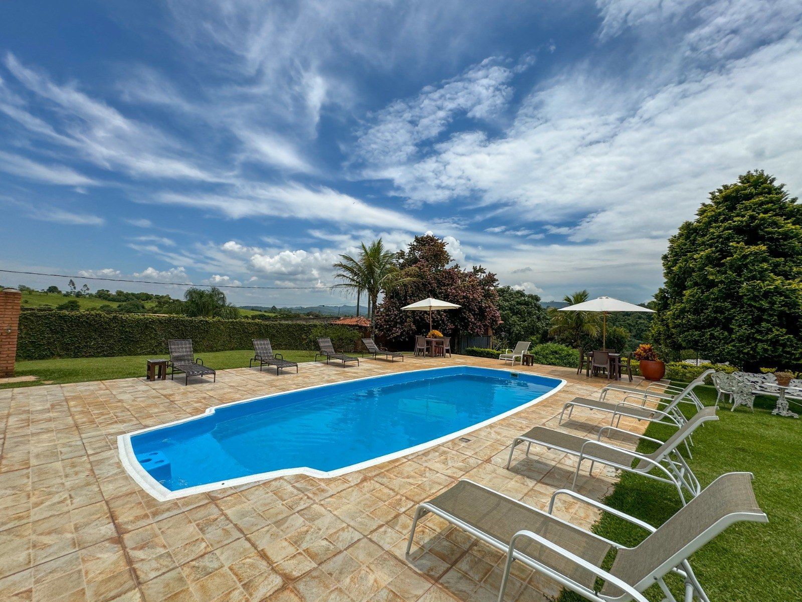 Piscina com água azul e espreguiçadeiras num dia ensolarado.