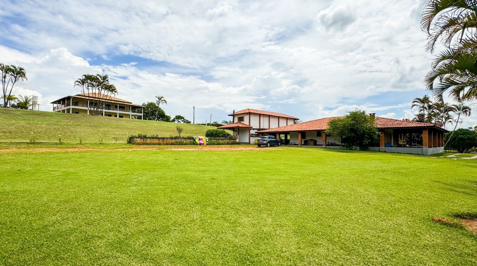 Gramado verdejante com uma casa grande e outras construções sob um céu parcialmente nublado.