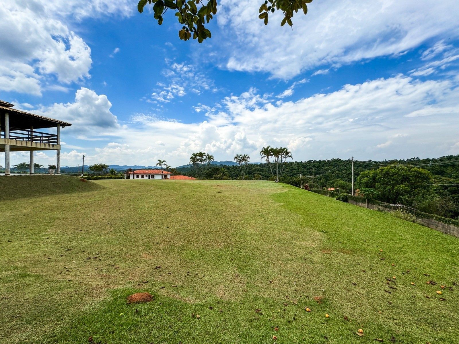 Gramado verdejante com um prédio no alto de uma colina sob um céu azul com nuvens.