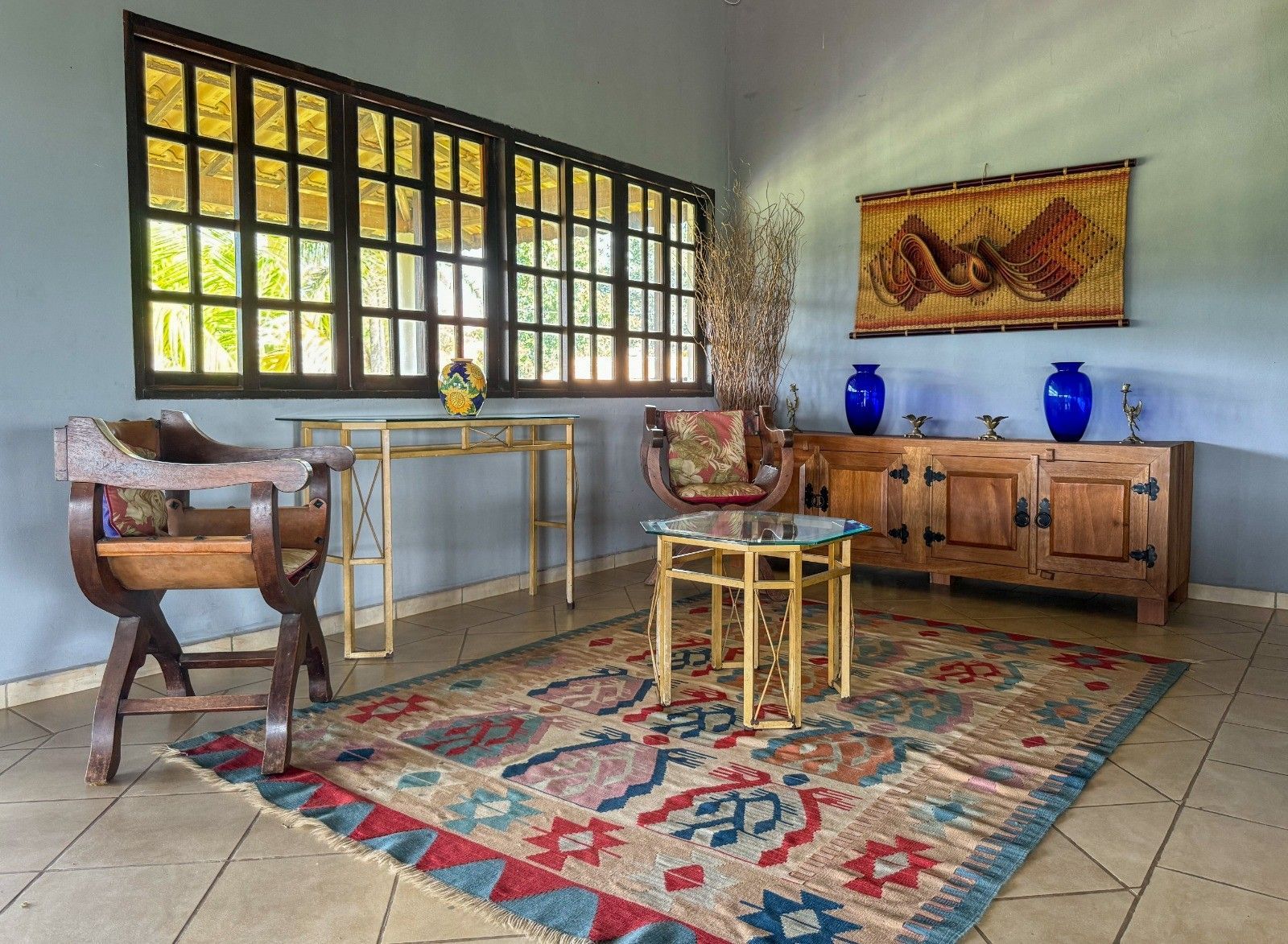 Quarto com tapete, móveis de madeira e paredes azuis. Janela e objetos decorativos presentes.