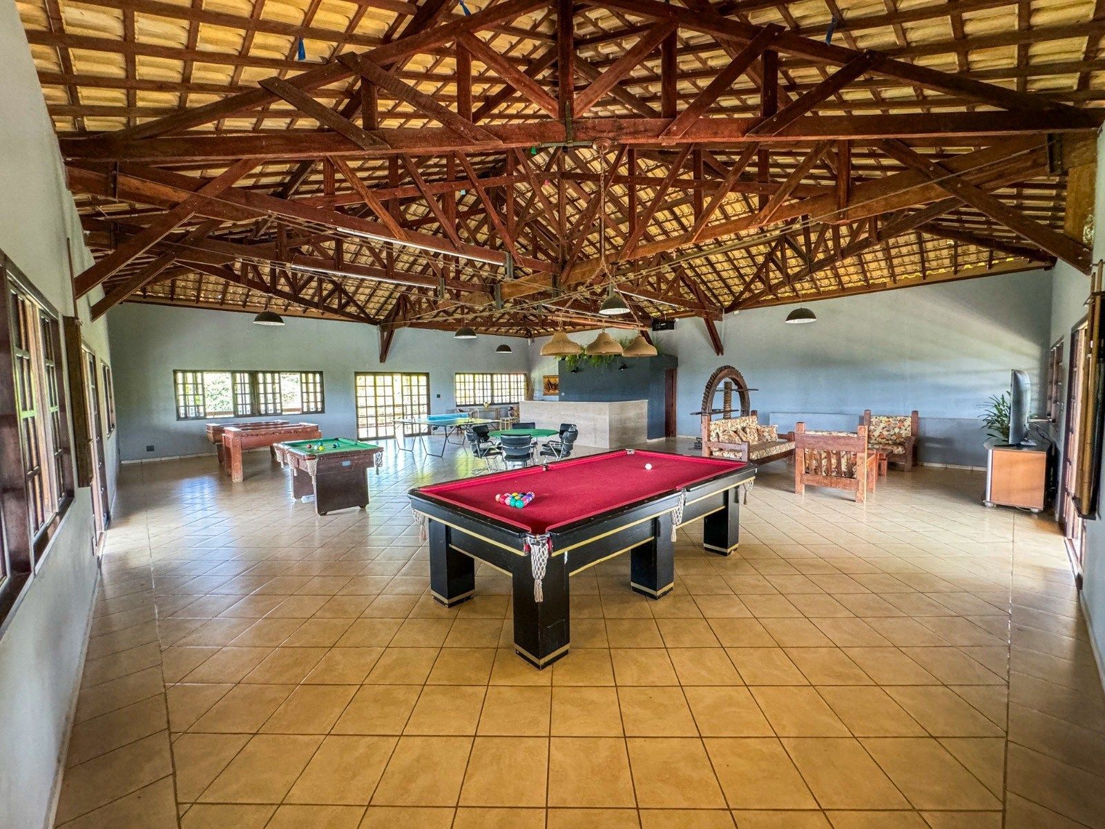 Interior de uma sala de jogos com mesas de bilhar, teto de madeira e assentos.