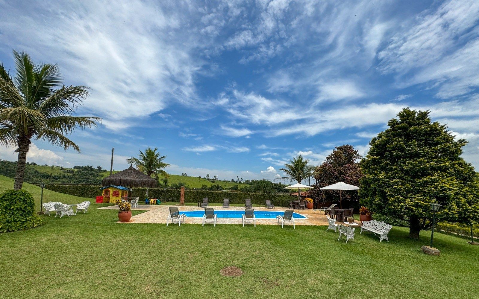 Área da piscina e pátio com gramado verdejante e céu ensolarado.