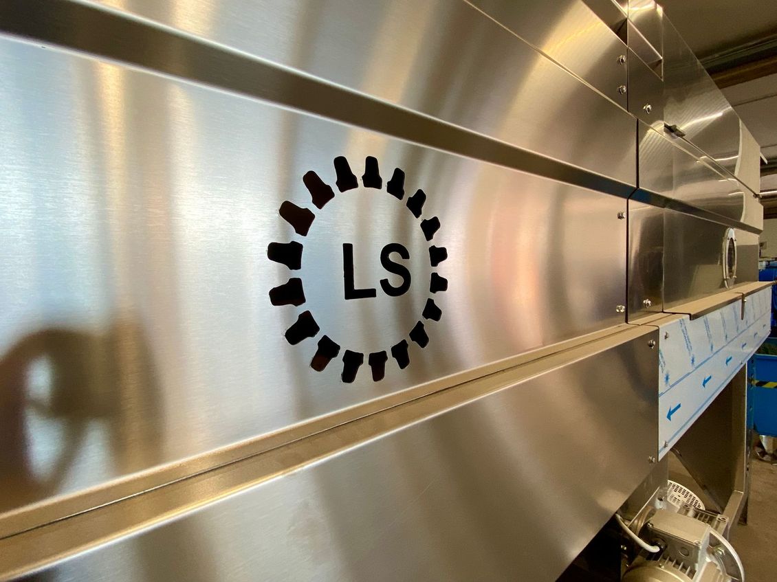 Primo piano di un pannello industriale in metallo spazzolato con logo LS circolare nero e bulloni.