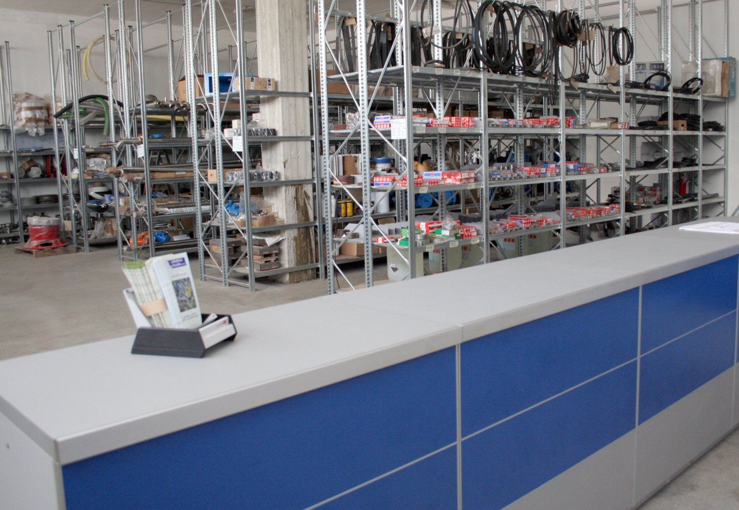 Comptoir de service bleu dans un magasin avec des étagères métalliques remplies de marchandises derrière.