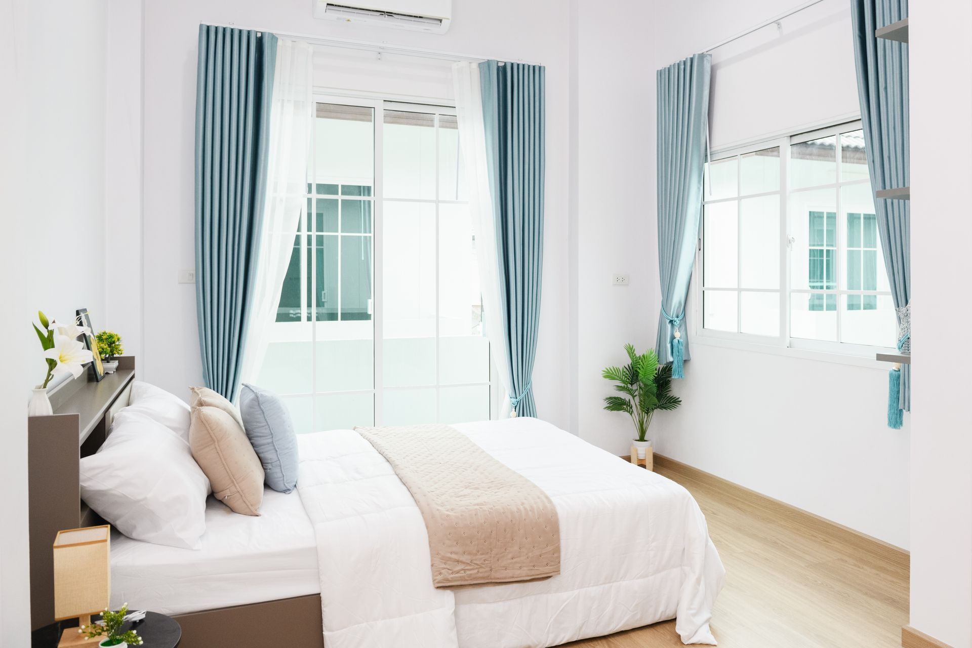 Camera da letto luminosa con letto bianco, tende blu e un'ampia finestra che lascia entrare la luce naturale.