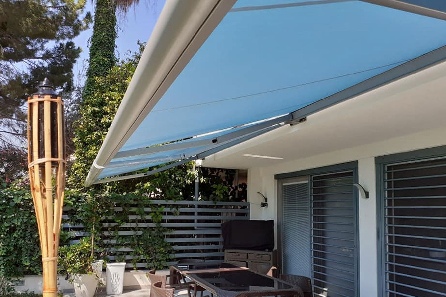 Patio con tenda da sole blu retrattile estesa sopra i posti a sedere all'aperto accanto a una casa