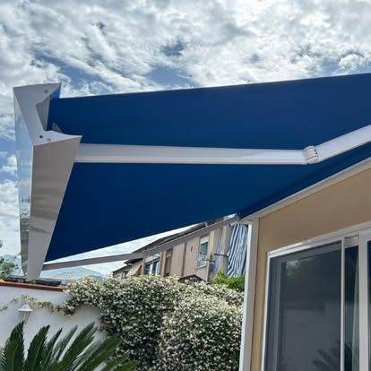 Tenda da sole blu retrattile estesa su un patio accanto a una casa e al giardino sotto un cielo nuvoloso