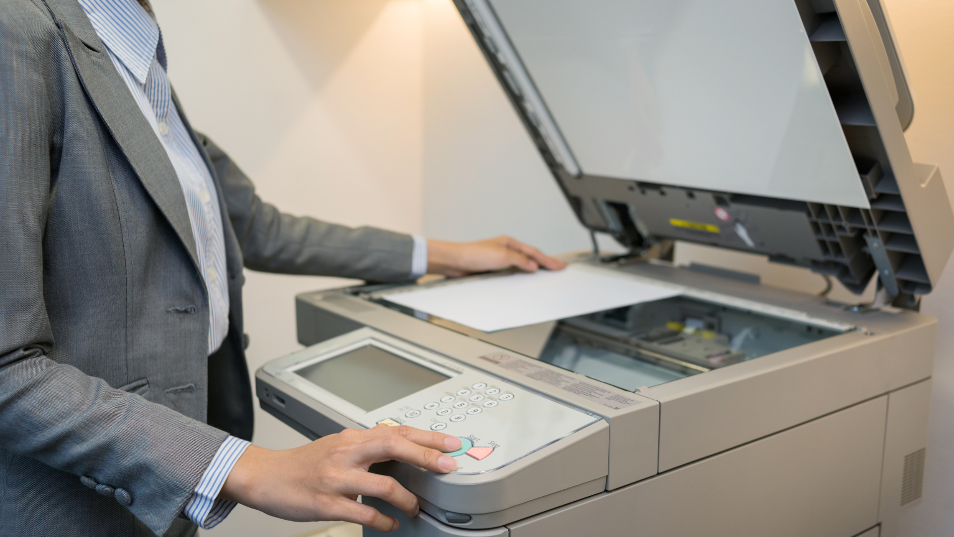 Person in a grey suit uses a copier, placing a white paper on the scanner bed.