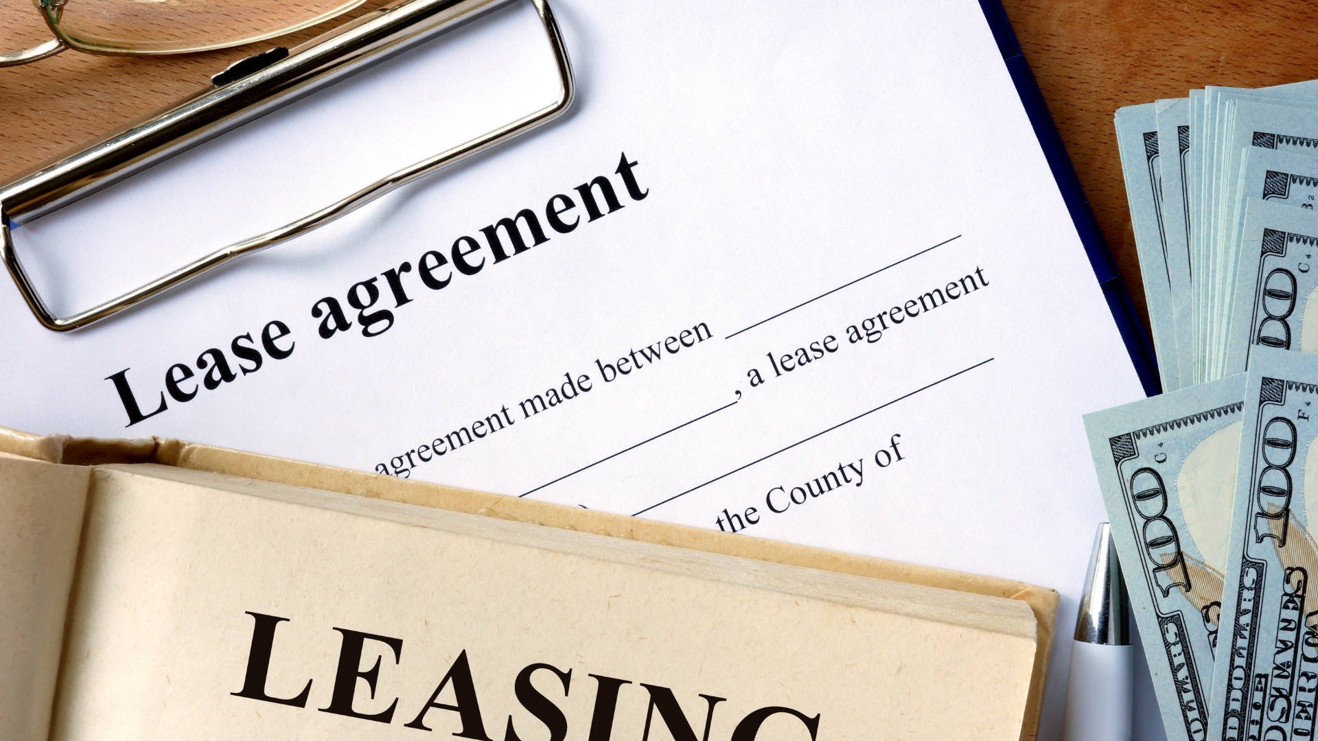 Lease agreement on clipboard, cash, and leasing book on a wood table.