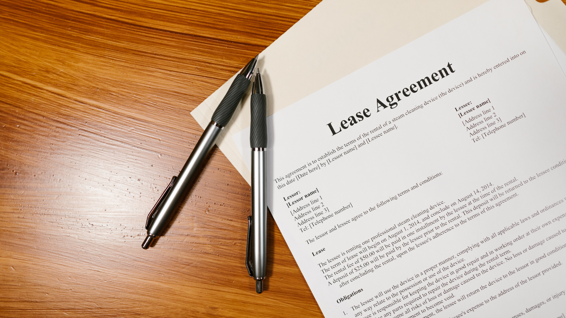 Lease agreement document on a wooden table, with two pens resting on top.