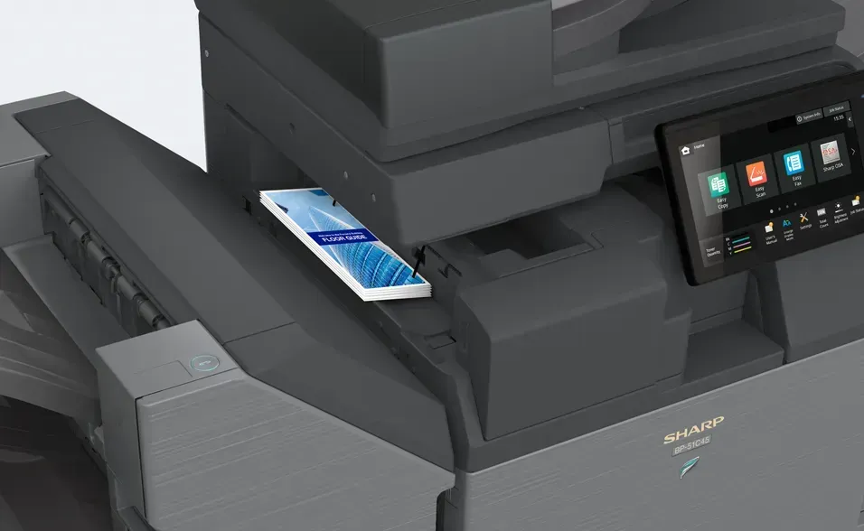 Smartphone resting on a Sharp multifunction printer; black and gray, screen showing interface.