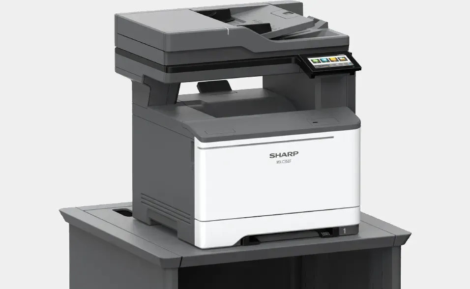 A Sharp color multifunction printer on a gray desk against a light background.