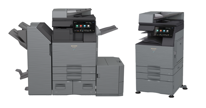 Two large gray office photocopiers. One has multiple trays and a large paper-handling attachment.