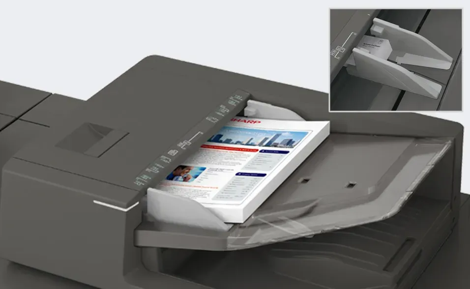 A printer's output tray holding a stack of printed documents. Close-up shows angled output guides.