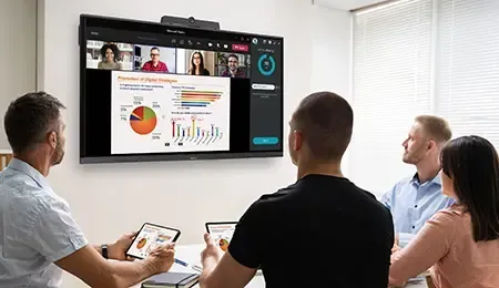 People in a meeting room watching a presentation on a large screen with remote participants.