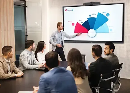 People in a meeting room watching a presentation on a large screen with remote participants.
