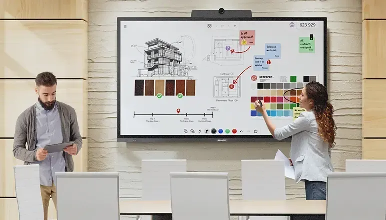 Two people in a modern office using a digital whiteboard with architectural designs.