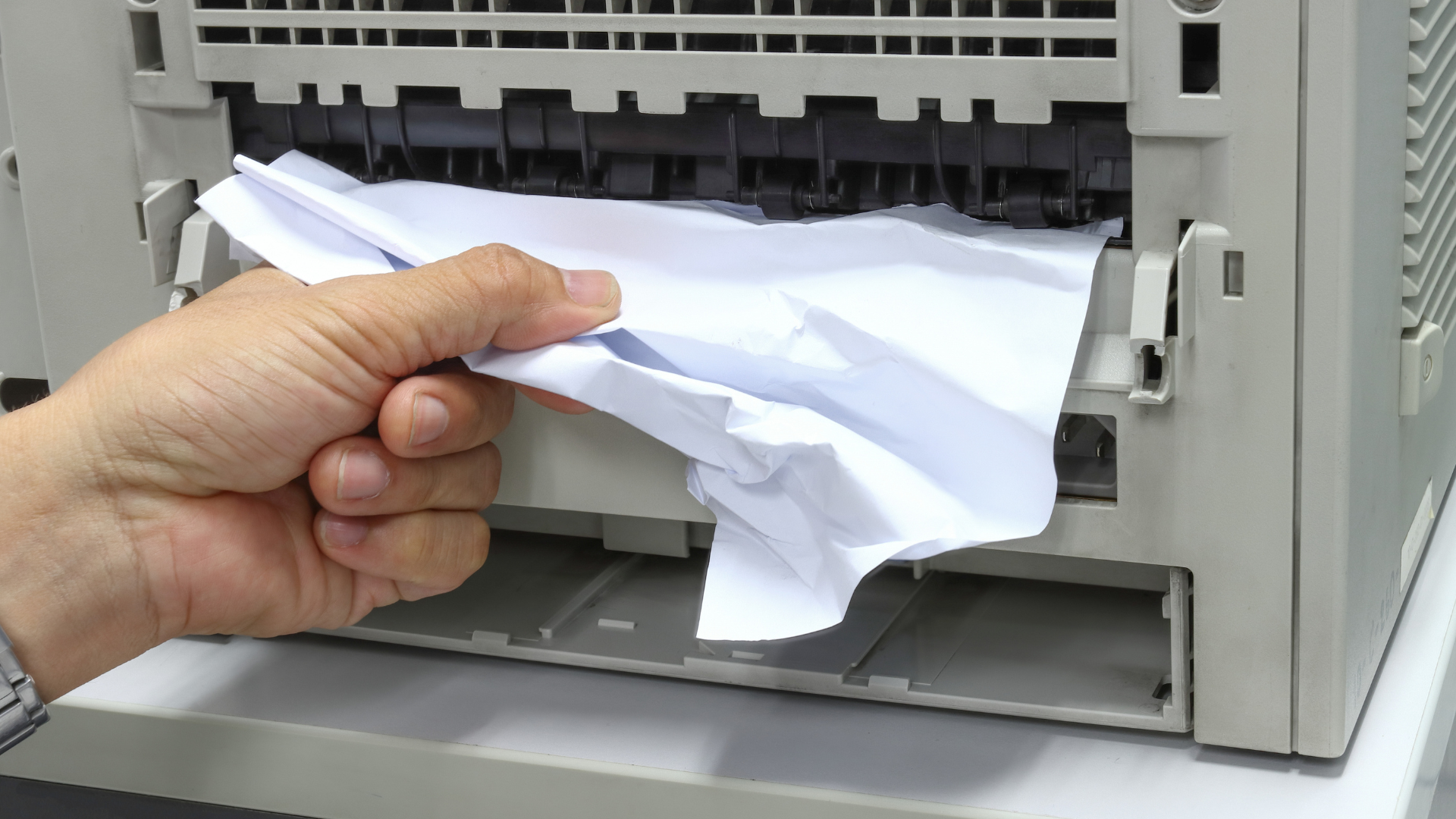 Person removes crumpled paper from a printer, likely clearing a paper jam.