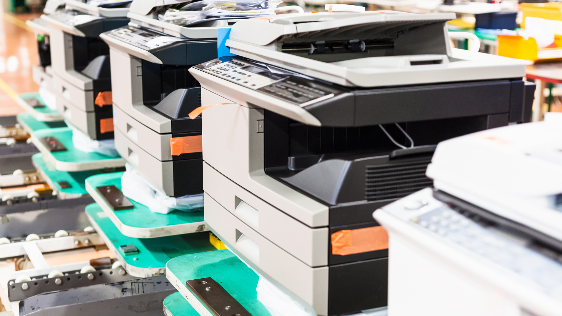 Row of printers on an assembly line, showing black and gray machines with orange accents.