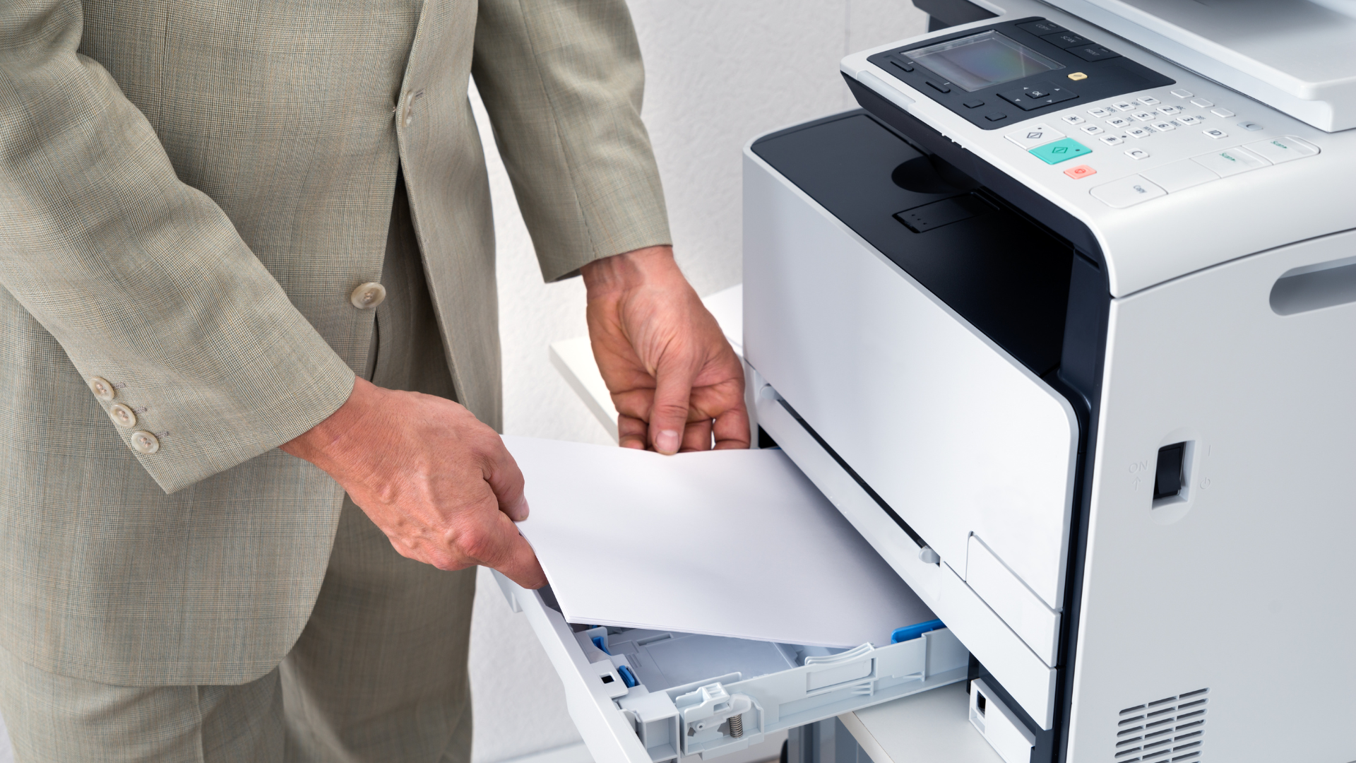 Man in suit loading paper into a white office printer.