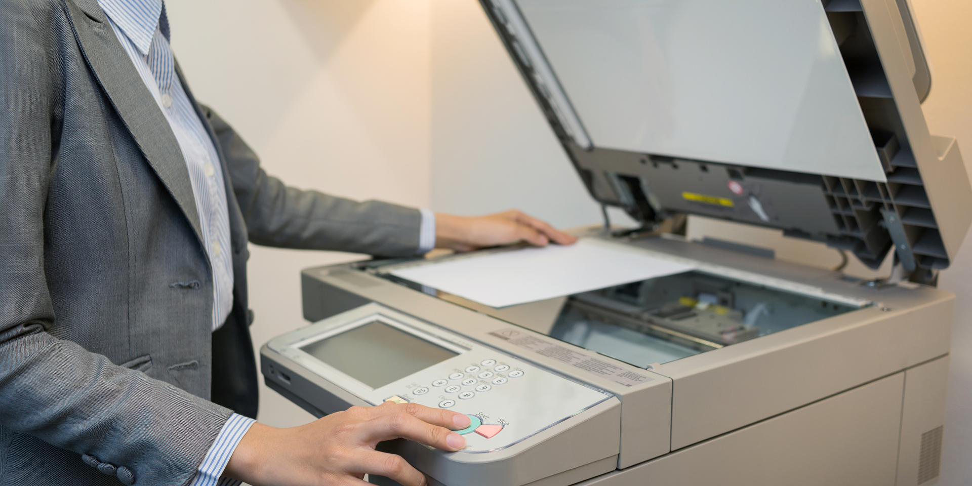 Person in a business suit placing a sheet of paper on a photocopier.