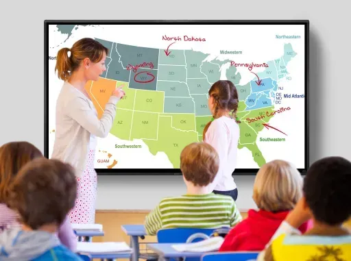 Teacher and student at a classroom screen, pointing at a map of the United States. Students watch.