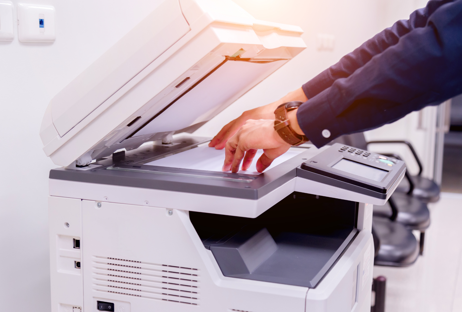 Person placing paper on a copier machine, hands visible. Office setting with bright light.