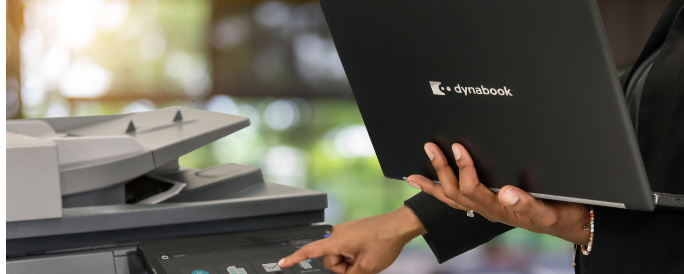 Person using a photocopier and laptop, possibly printing or copying documents.