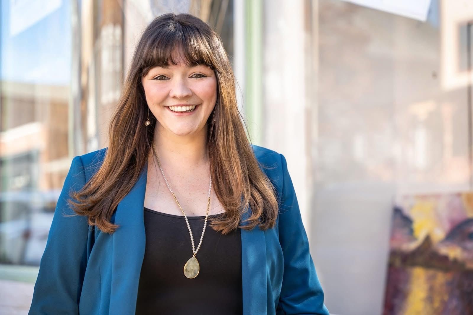 A Woman with long dark hair walks in the sun smiling