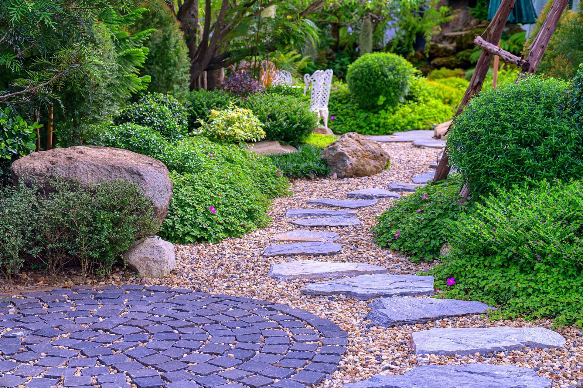 Stone garden path winding through lush green shrubs and trees with stepping stones and gravel.