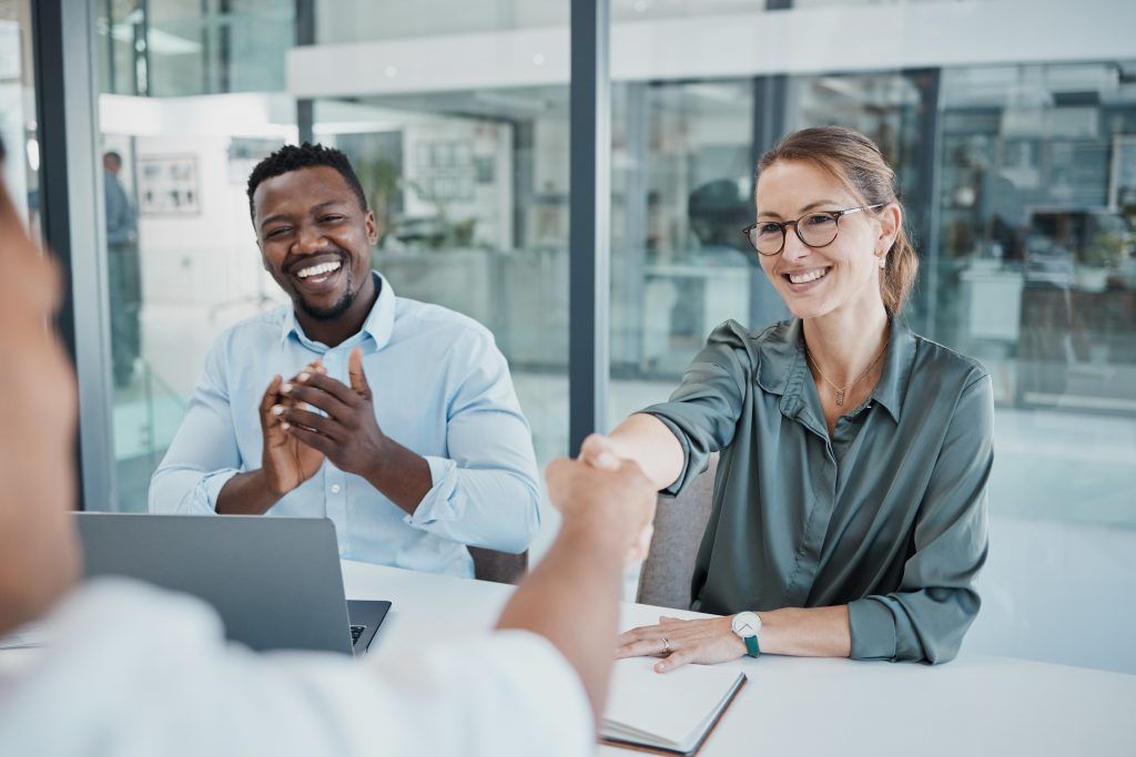 Um homem e uma mulher apertam as mãos enquanto estão sentados à mesa.