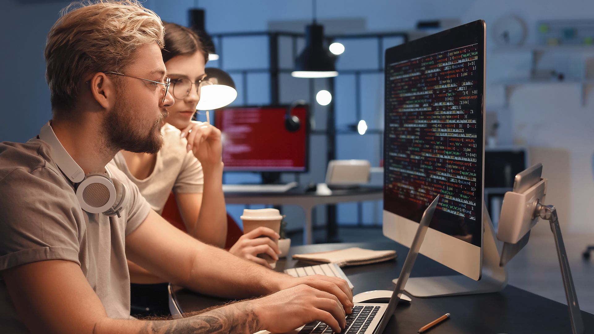 Dois profissionais de TI alocados em uma empresa trabalhando na frente de um computador.