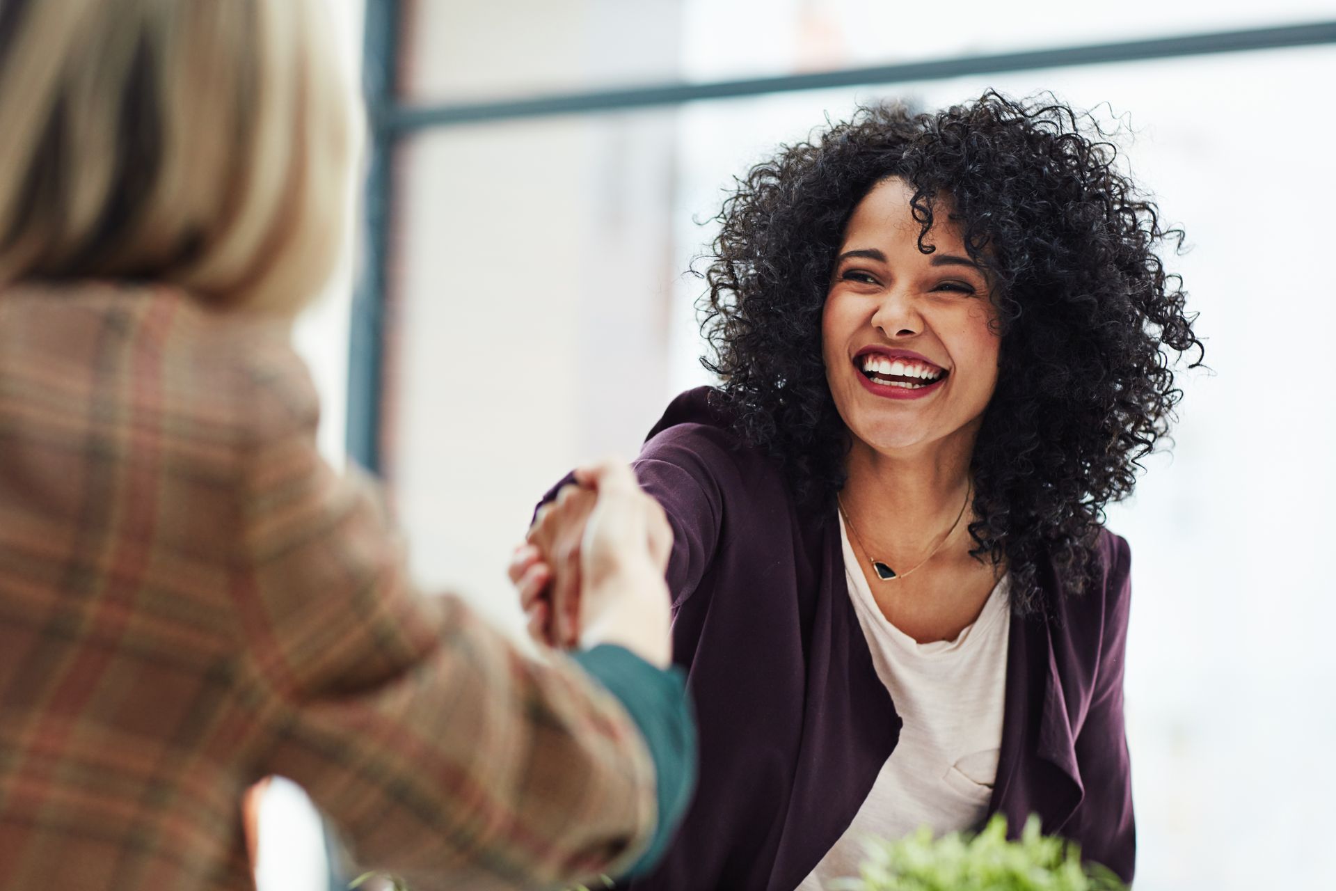 Duas mulheres apertando as mãos e uma sorrindo