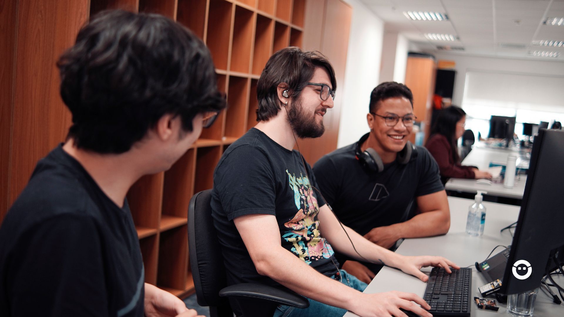 Um grupo de jovens está sentado em uma mesa em frente a um computador.