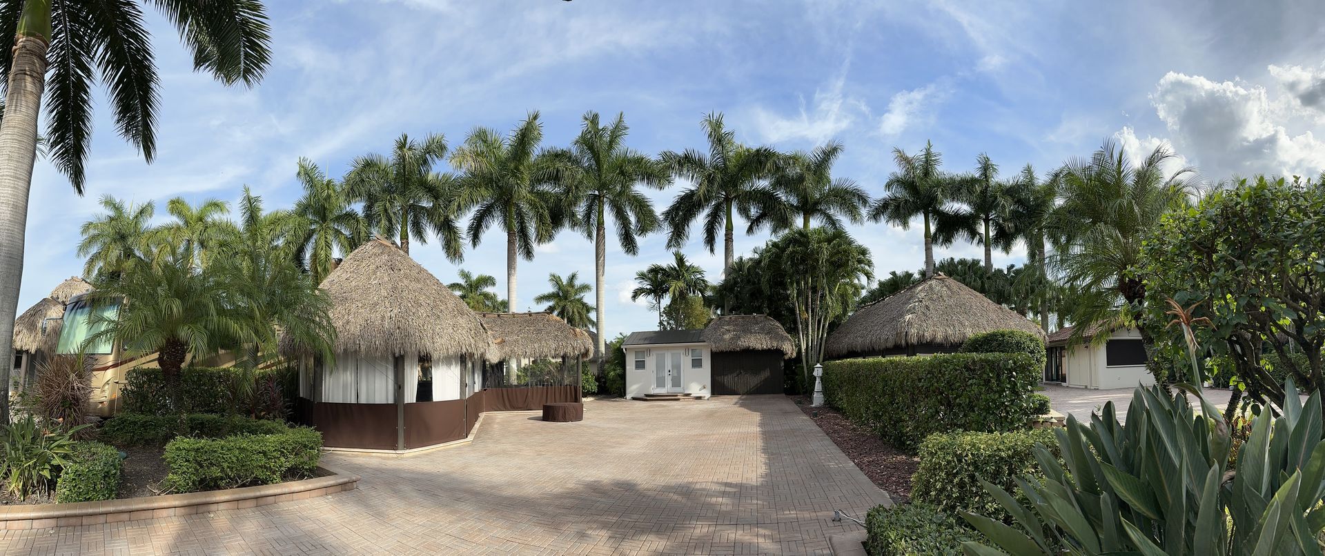 A panoramic view of a house with thatched roofs surrounded by palm trees.