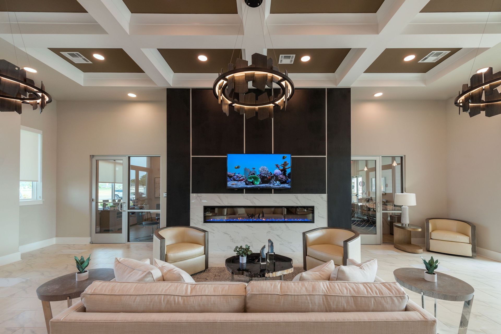 Lounge area with fireplace, TV, seating, and decorative lighting in a building with glass doors and a coffered ceiling.