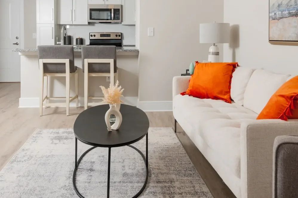 Living room with white sofa, orange pillows, black coffee table, and kitchen bar with stools.