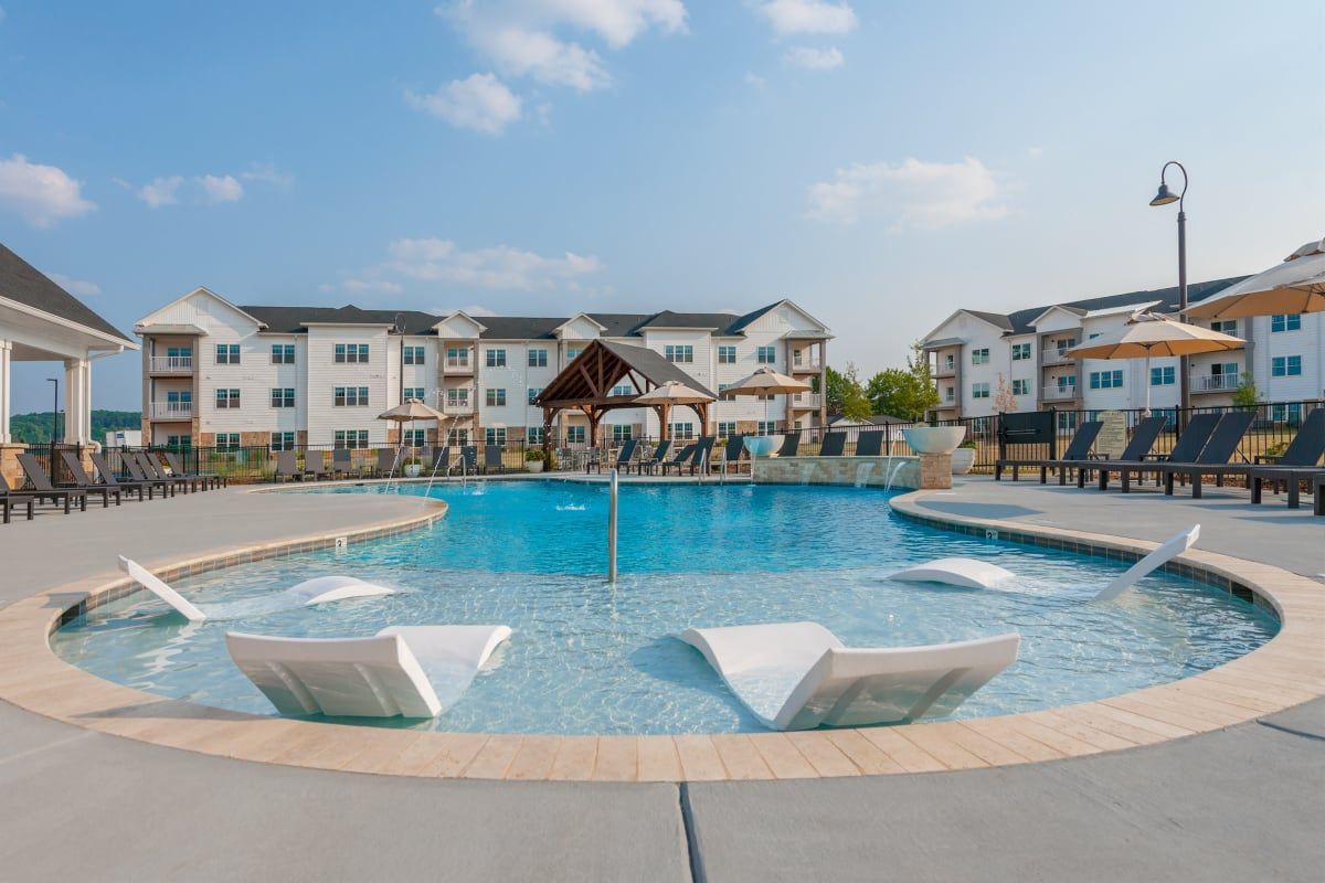 Swimming pool with lounge chairs, building in background, sunny day.