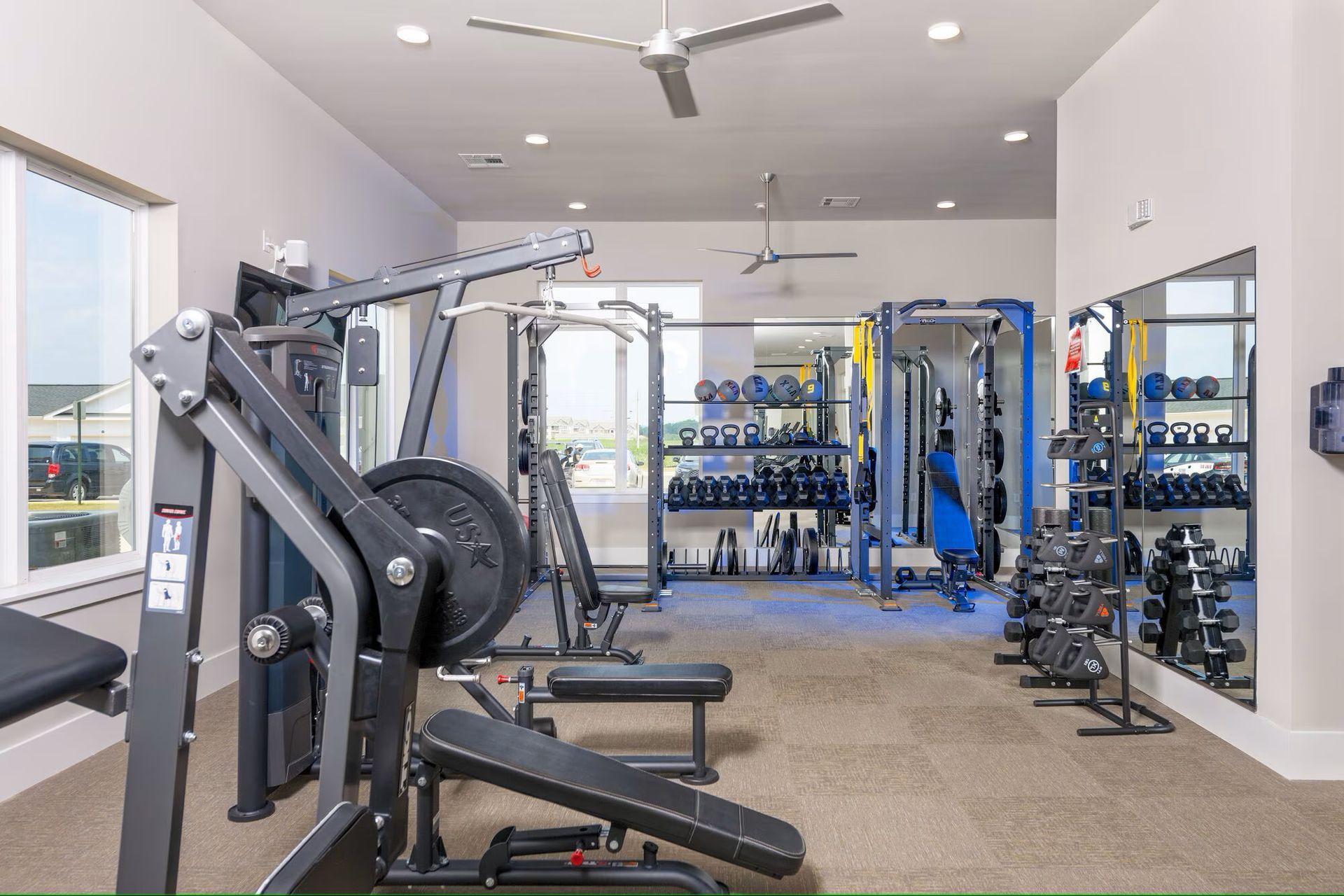 Gym with weight machines, dumbbells, mirrors, and ceiling fans.