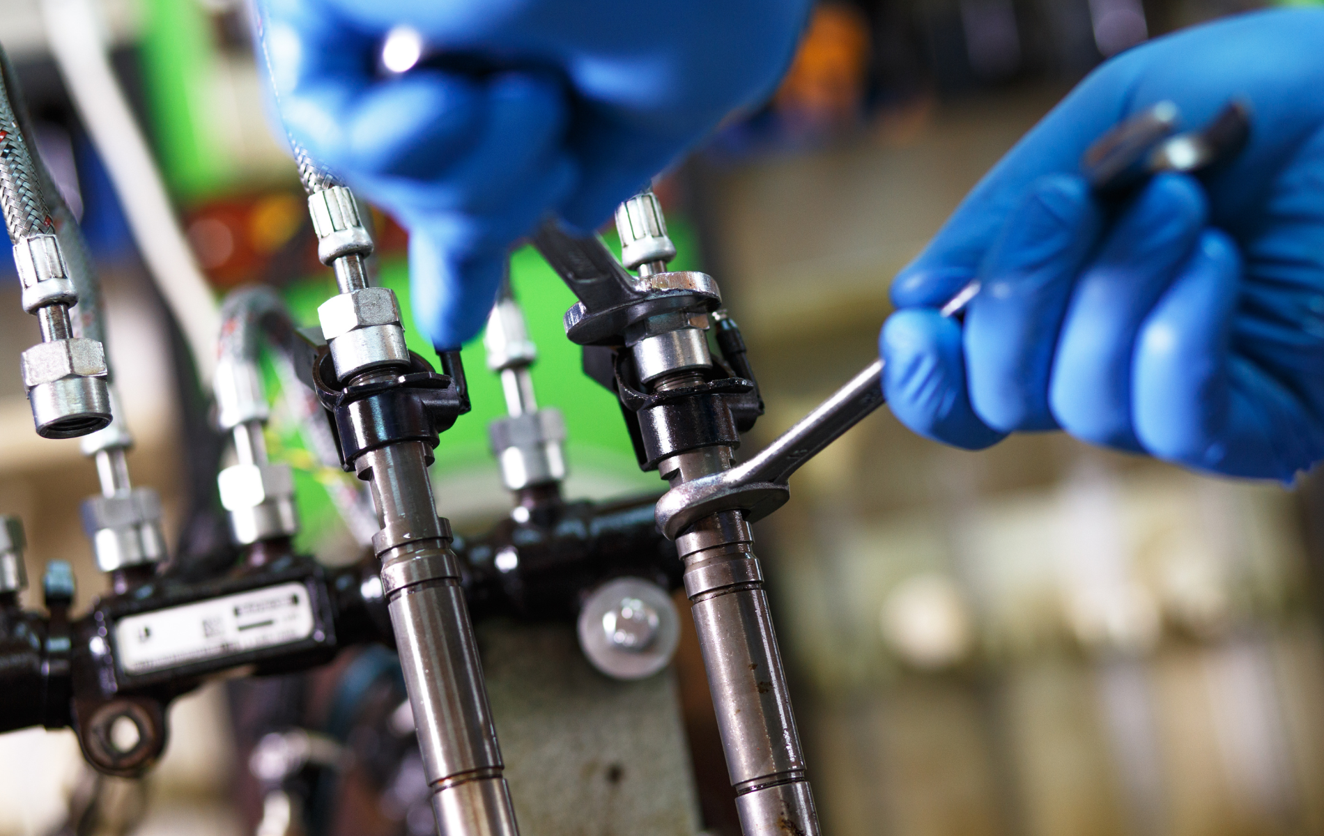 Hands in blue gloves using a wrench on engine component in a repair setting.