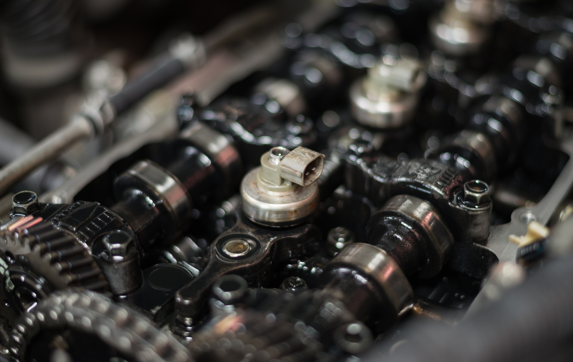 Engine parts, including camshafts, bathed in oil, viewed close-up.
