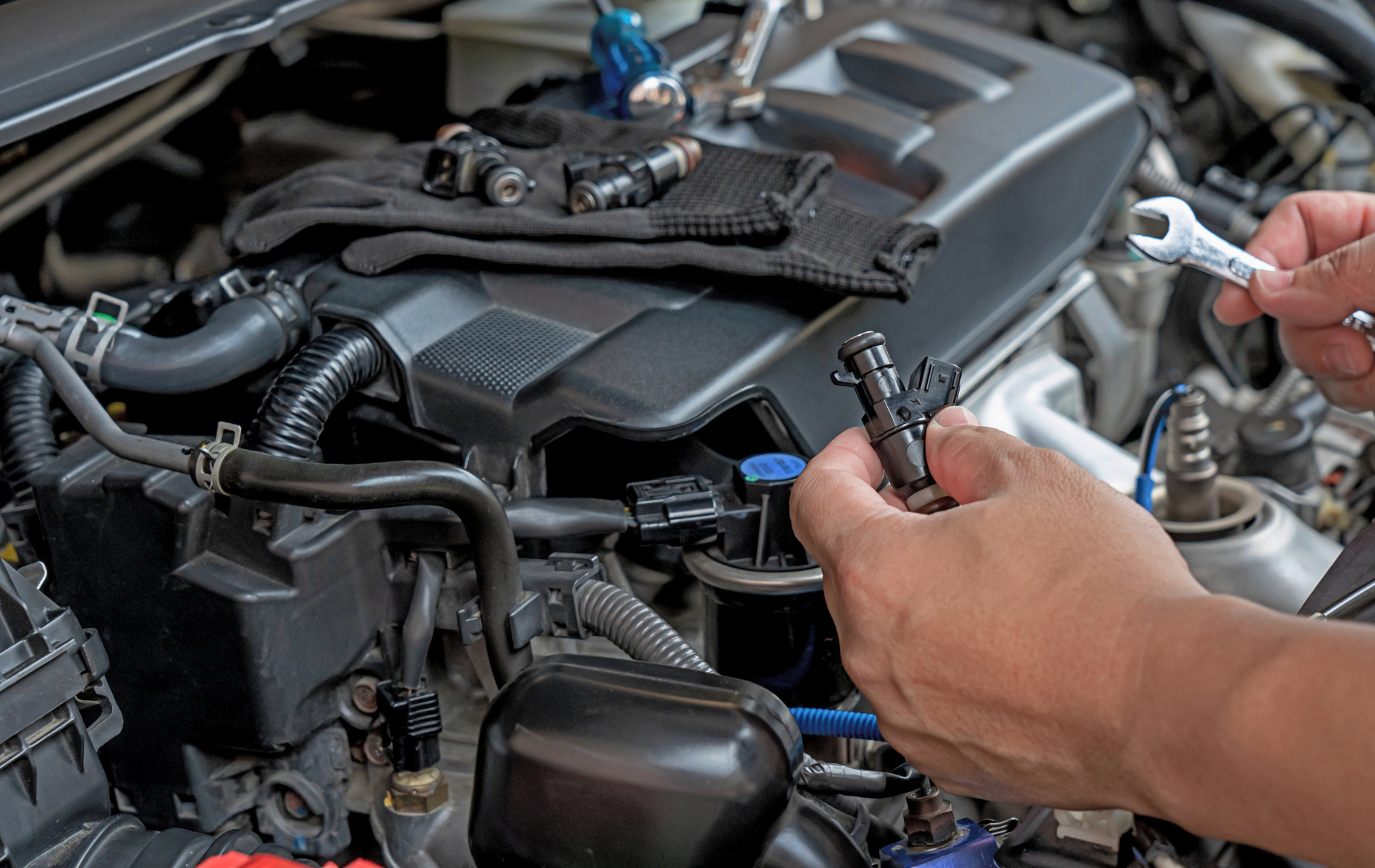 Mechanic working on a car engine, holding fuel injectors and a wrench.