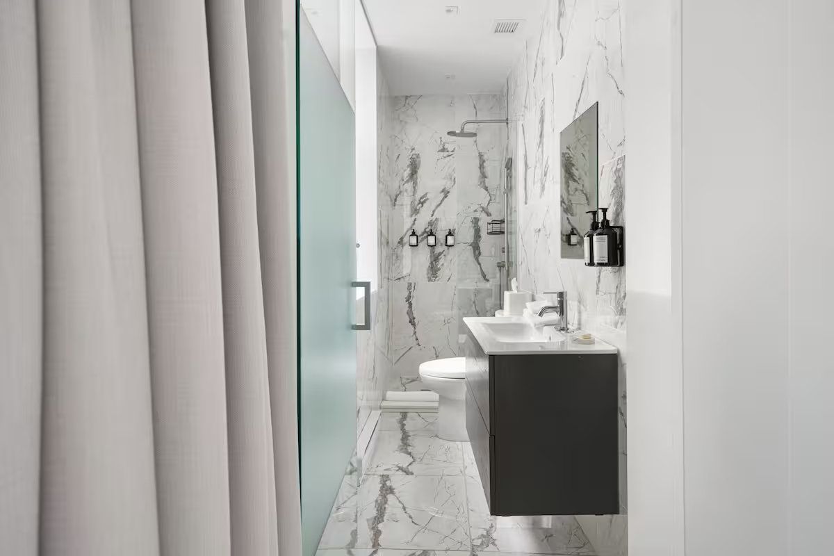 A modern, minimalist bathroom with white marble-patterned walls and floor, featuring a floating vanity and shower.