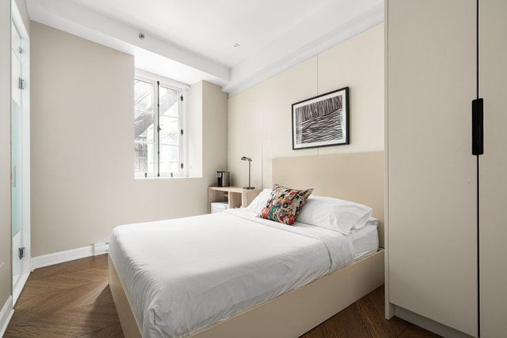 Beige bedroom with a bed, small desk, closet, and a window.