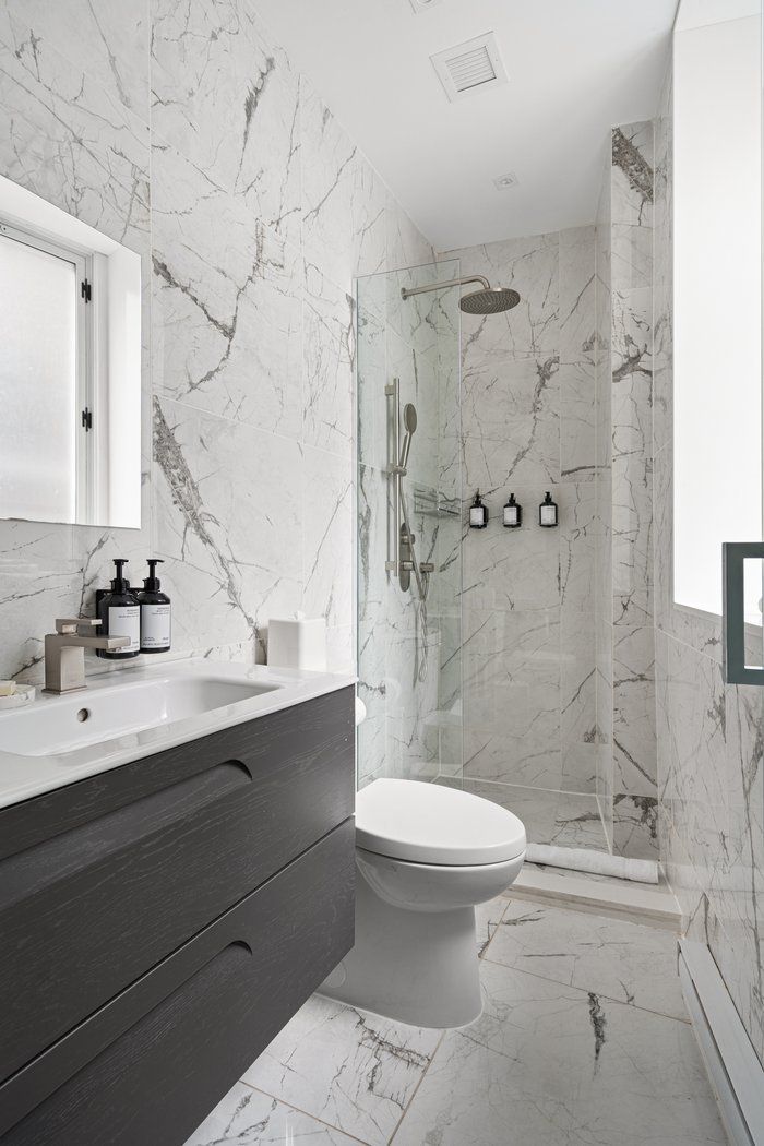 Marble-tiled bathroom with a glass shower, vanity with mirror, and toilet.