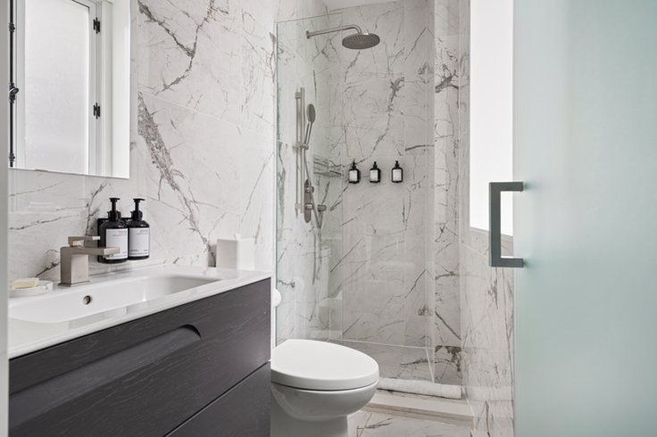 Modern bathroom with marble walls, shower, toilet, and sink.